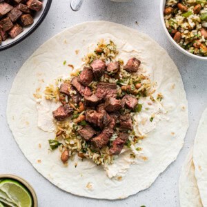 Beef tacos on a white table with limes and garnishes.