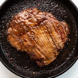 A steak is being cooked in a cast iron skillet.