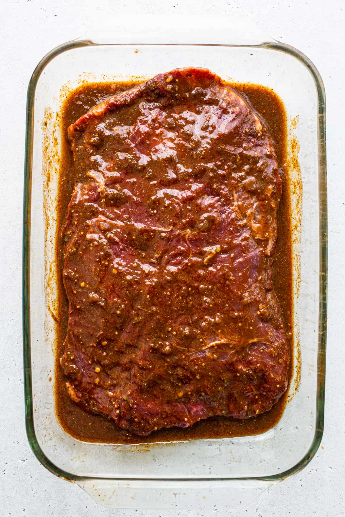 Flank steak marinating in a glass dish.