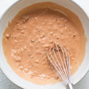 A bowl of sauce with a whisk in it.