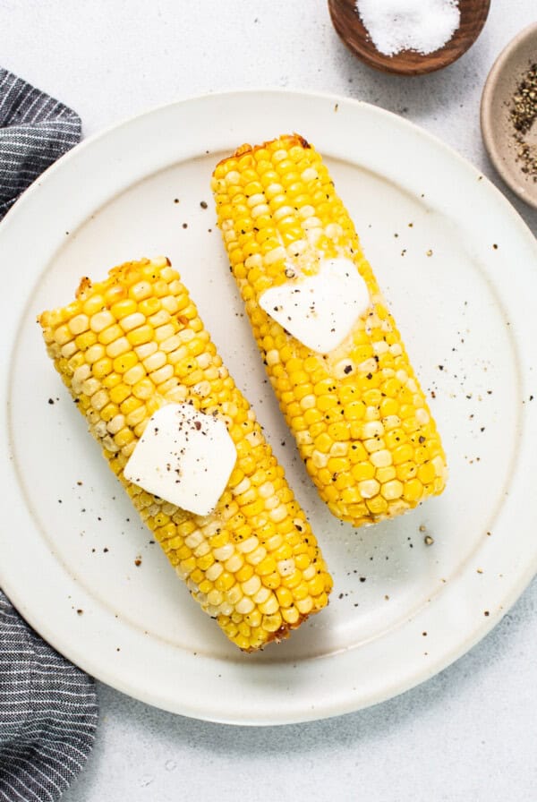 two corn on the cob with butter on top.