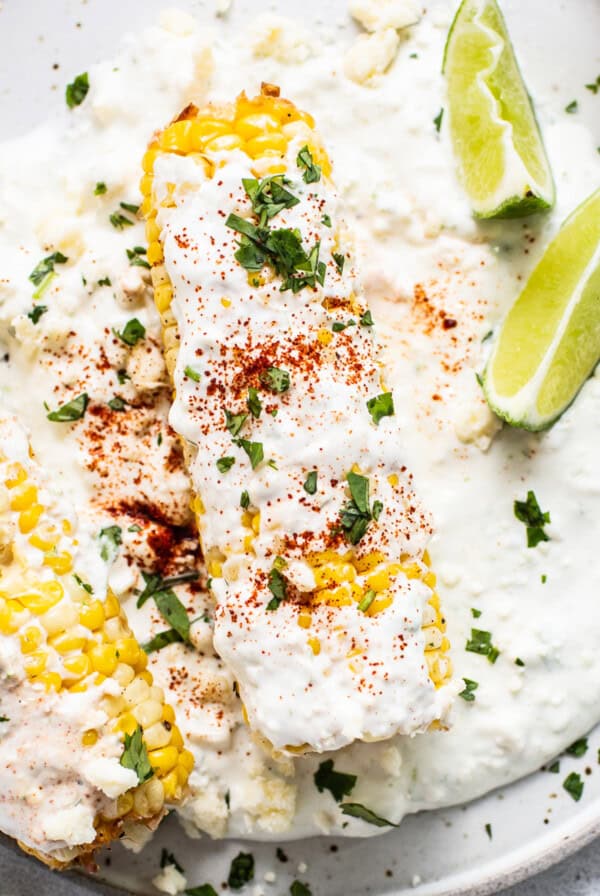 Air fryer elote on a plate with slices of lime.