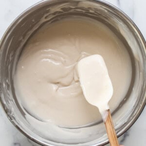 a hand holding a wooden spoon over a bowl of cream.