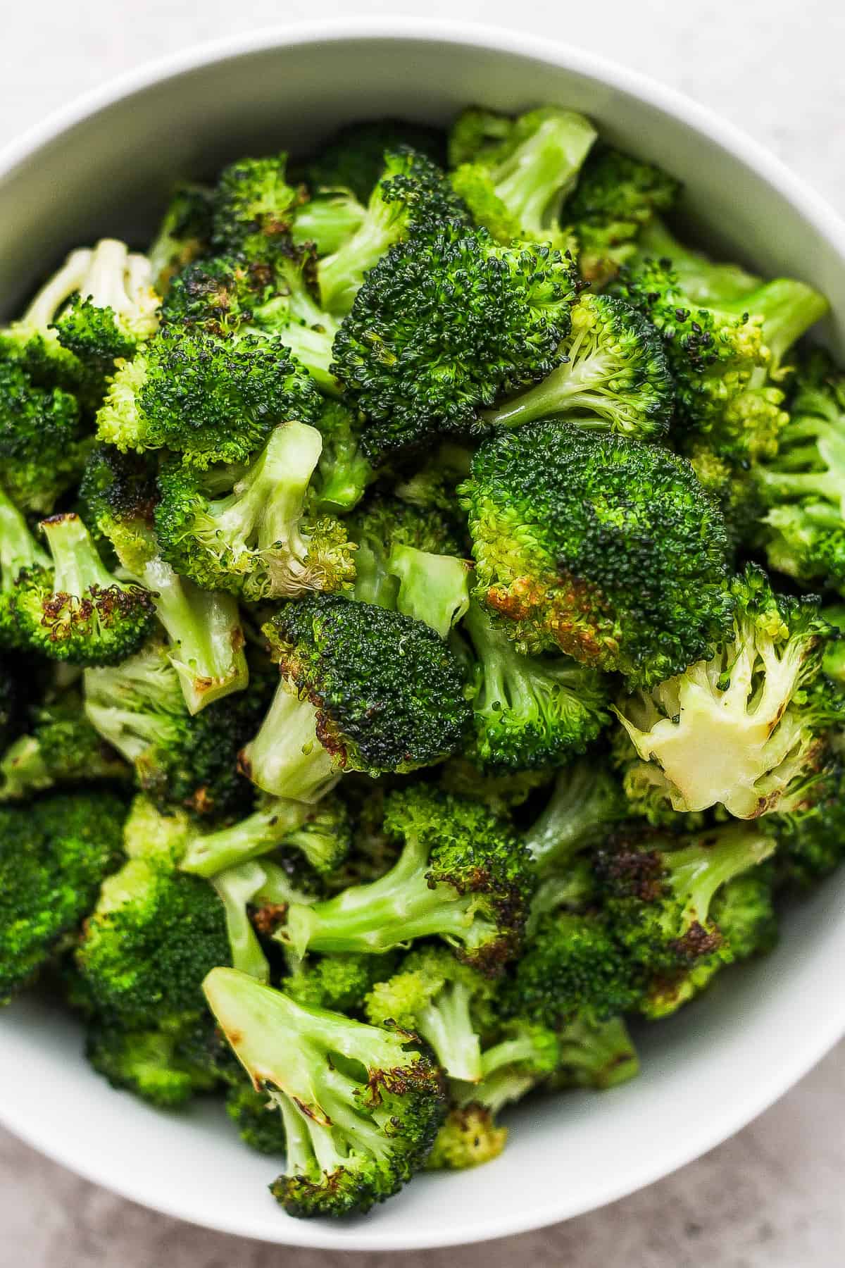 a white bowl filled with broccoli on top of a table.