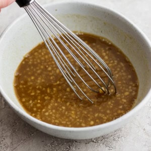 a hand holding a whisk in a bowl of brown liquid.