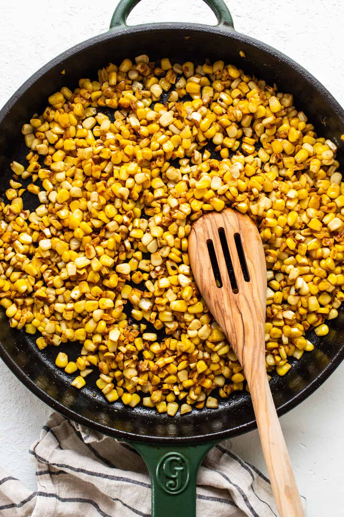 corn in a skillet with a wooden spoon.