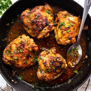 Chicken thighs in a skillet with sauce and herbs.