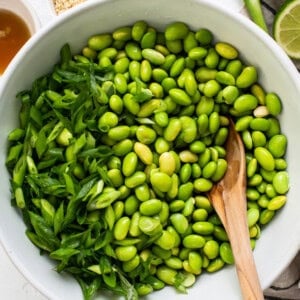 a white bowl filled with green beans and a wooden spoon.