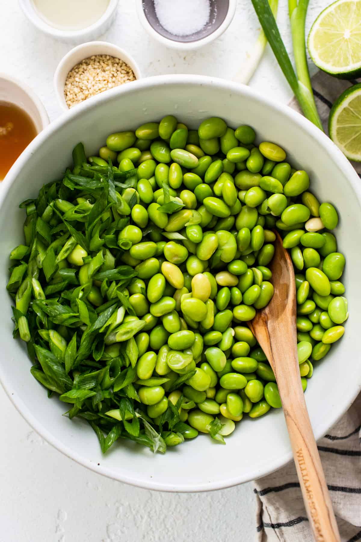 a white bowl filled with green beans and a wooden spoon.