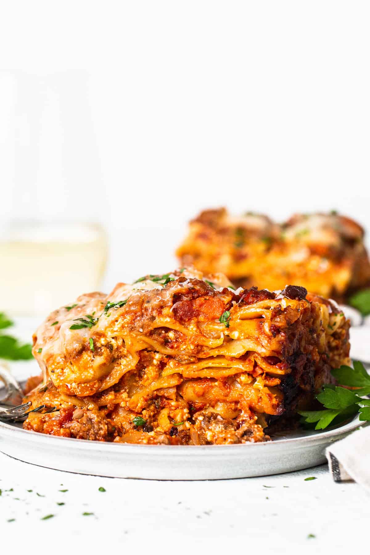 a white plate topped with lasagna next to a glass of wine.