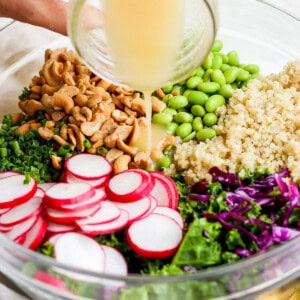 a person pouring dressing into a bowl of greens and radishes.