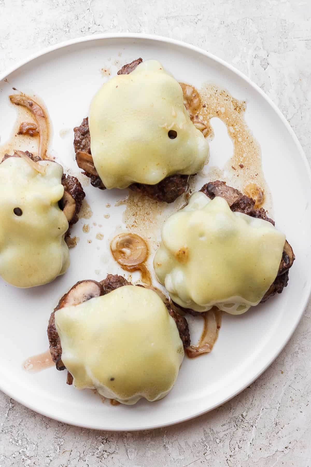 four mushroom burgers on a plate with sauce.