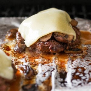 two burgers with cheese and mushrooms on top of foil.