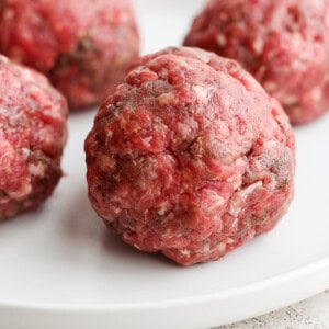 four meatballs on a white plate.