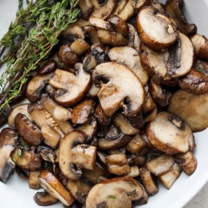 mushrooms in a white bowl with a sprig of thyme.