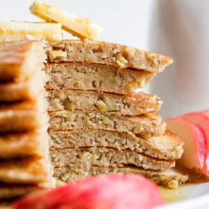 a stack of pancakes on a plate with apple slices.