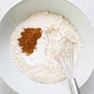 a bowl with flour, cinnamon, and a whisk.