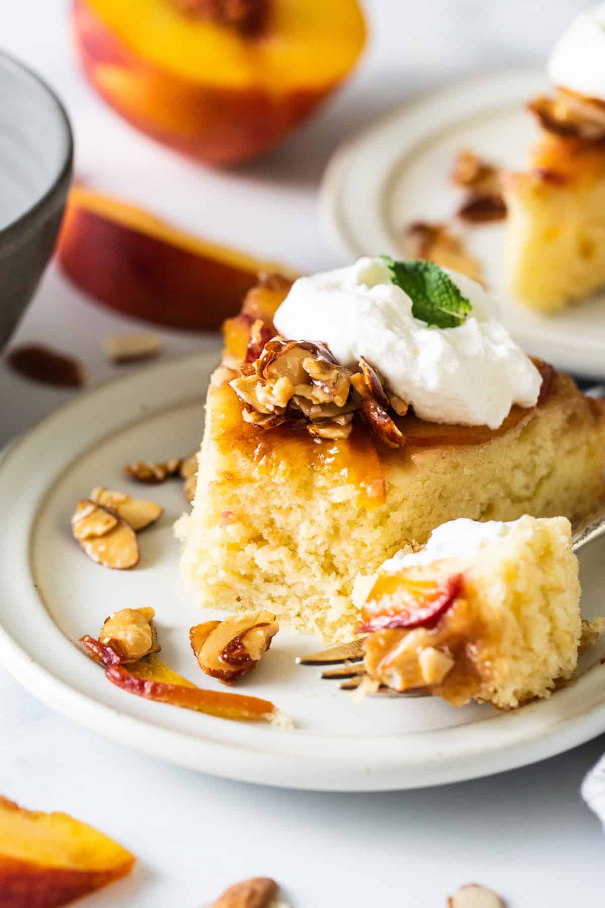 a slice of peach cake with whipped cream and almonds on a plate.