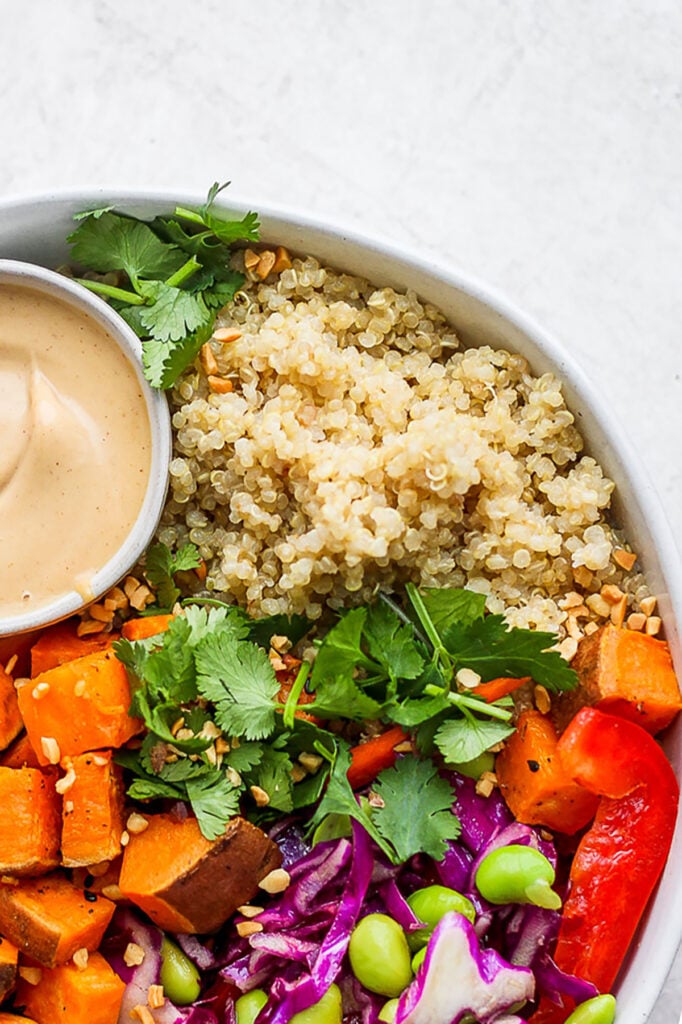 A bowl of coconut quinoa salad with a dipping sauce.