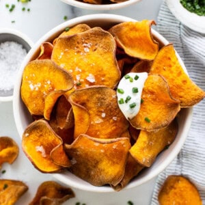 Sweet potato chips in a bowl with sour cream and parsley.