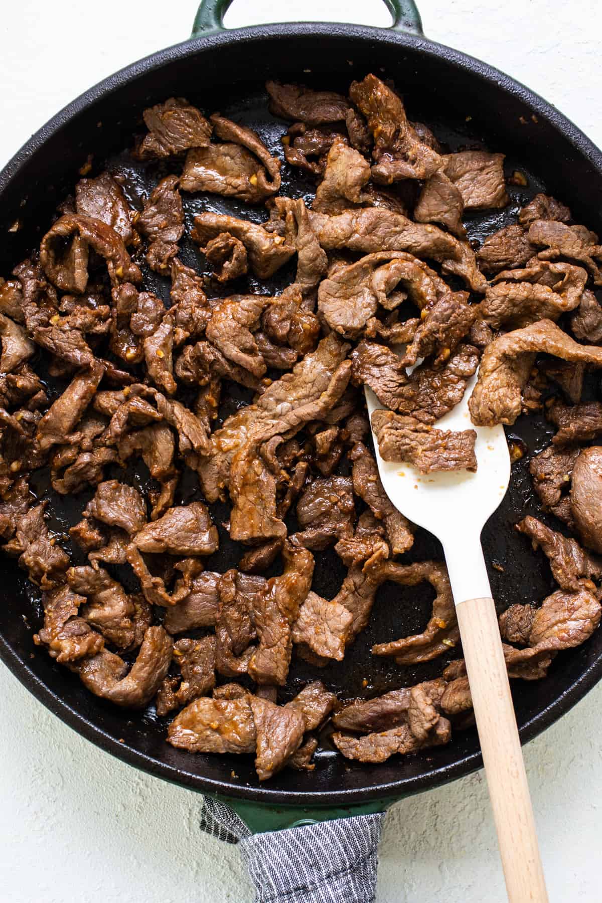 Beef in a skillet with a wooden spoon.