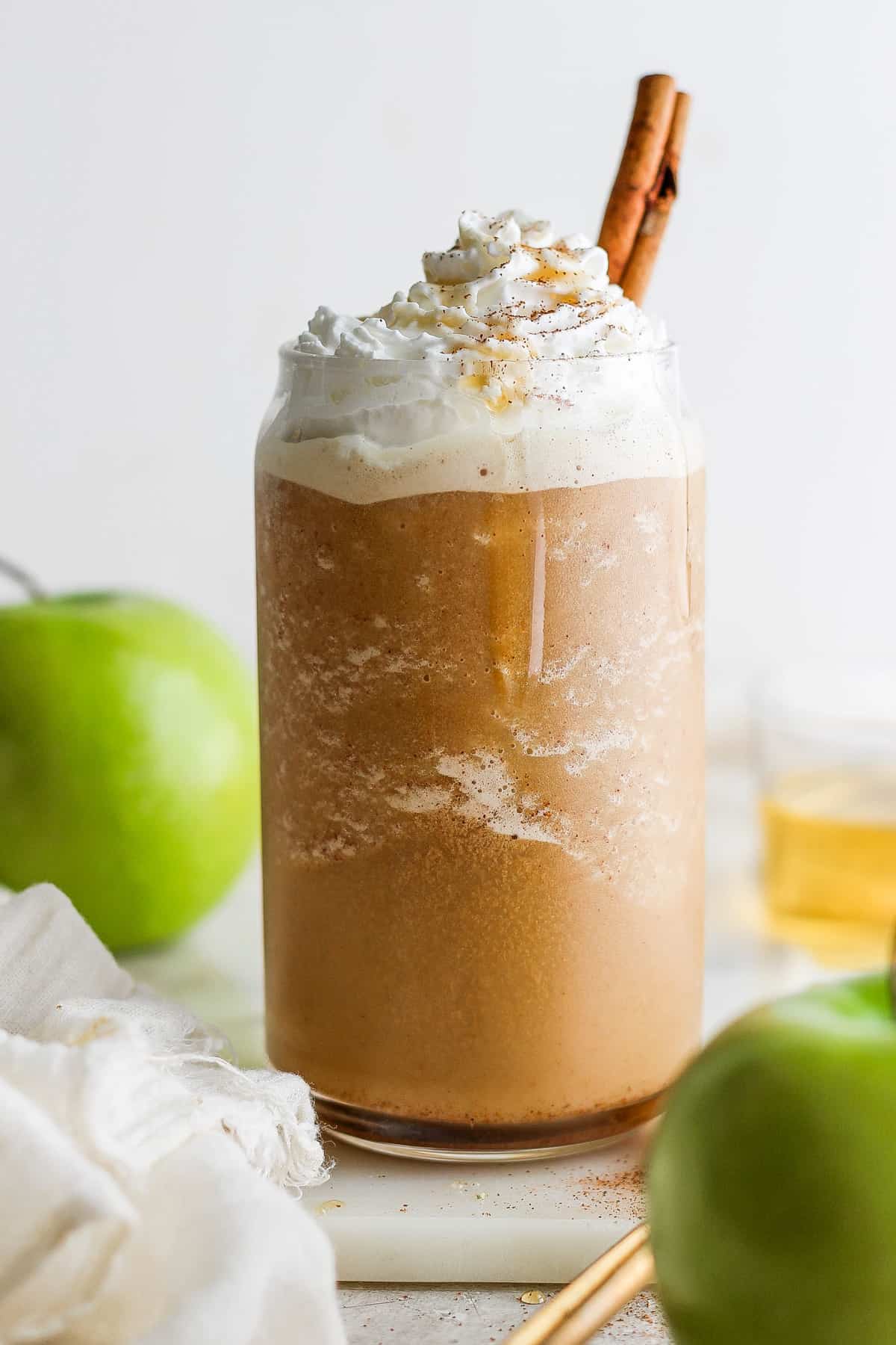 A mug with whipped cream, apples and cinnamon sticks.