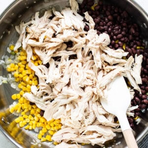 Chicken and corn in a pan with a wooden spoon.