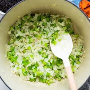 A pot full of onions and spices with a wooden spoon.