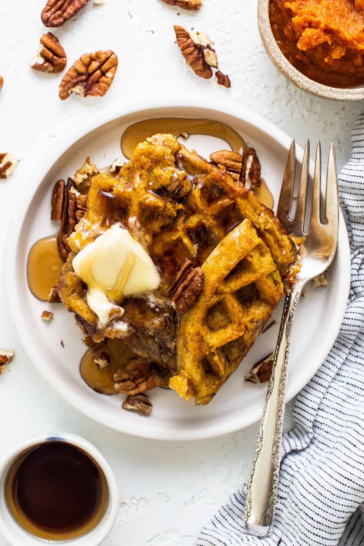 Pumpkin waffles with butter and pecans on a plate.