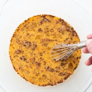 A person using a whisk to stir a cake on a plate.