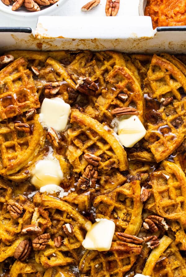 Pumpkin waffles in a baking dish with butter and pecans.