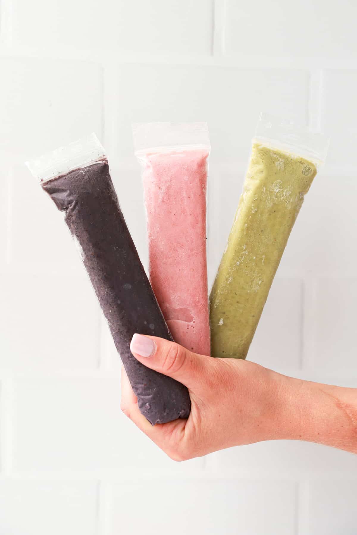 A hand holding three frozen popsicles.