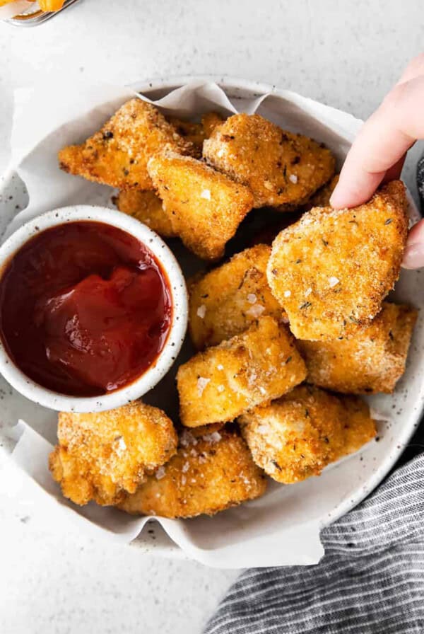 A person dipping chicken nuggets in ketchup.