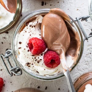 Chocolate mousse in jars with whipped cream and raspberries.