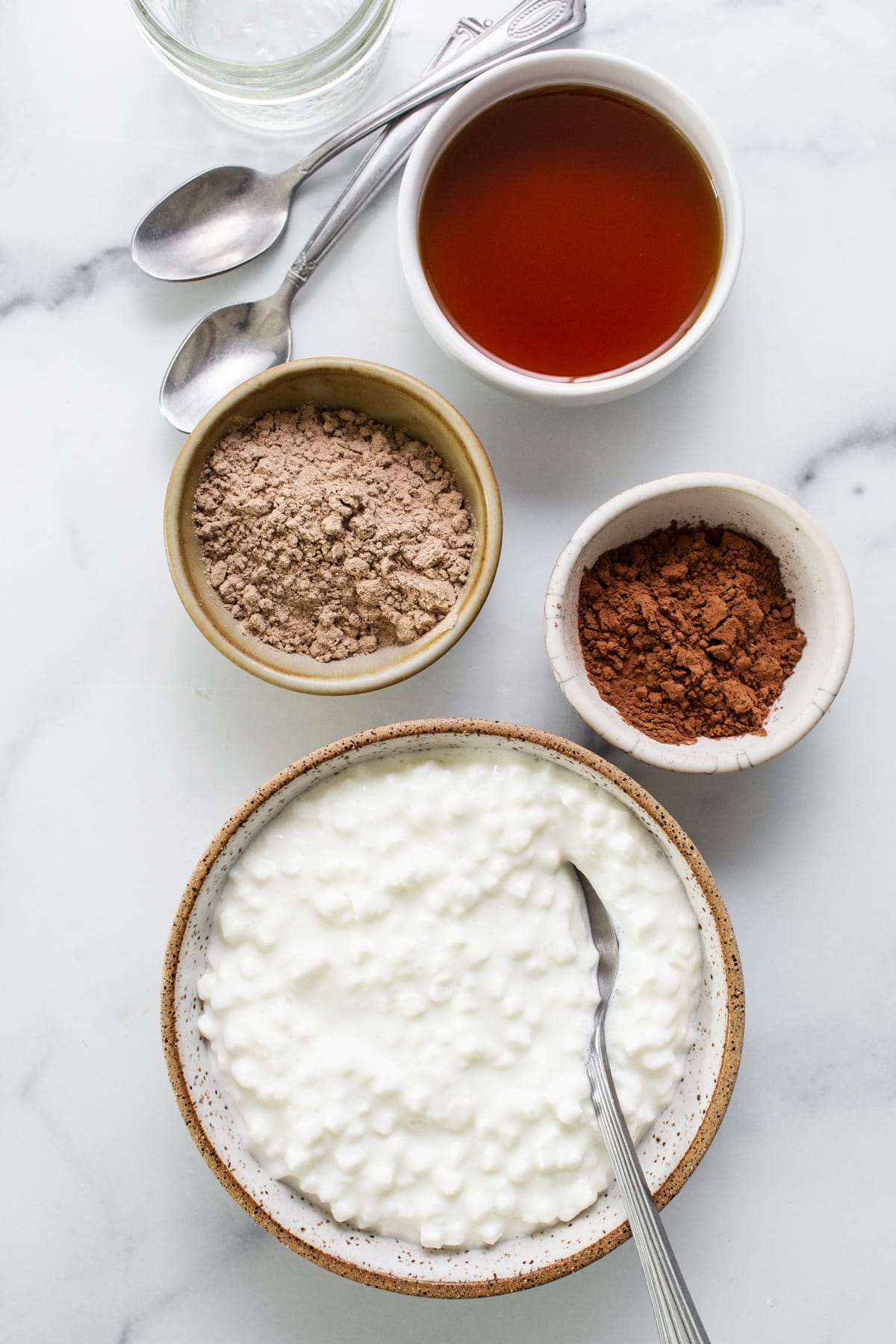 A bowl of yogurt with ingredients on a marble table.