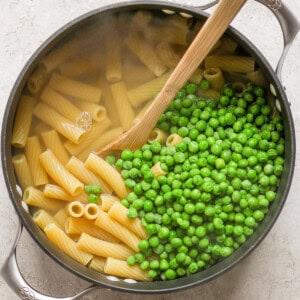 Peas and pasta in a pan with a wooden spoon.