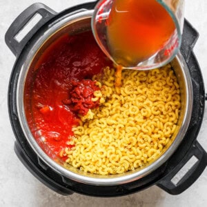 A person pouring sauce into a pot of pasta.