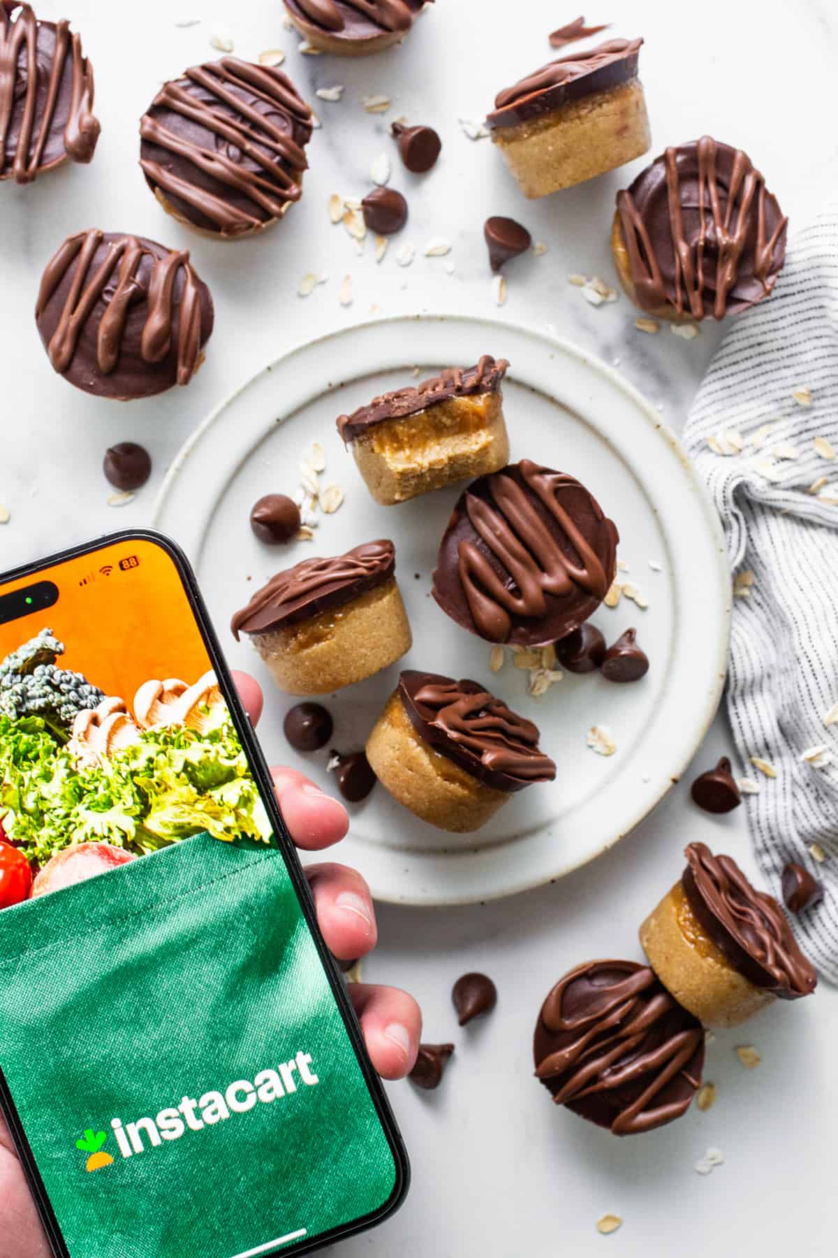 A person holding a smartphone with a plate of cookies and brownies.