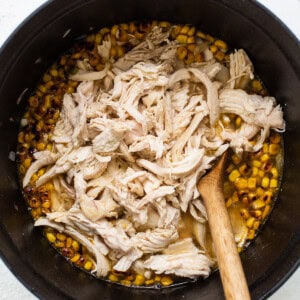 Chicken and corn in a pan with a wooden spoon.