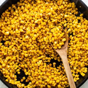 Corn in a skillet with a wooden spoon.