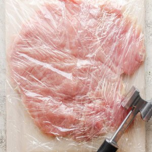 A piece of meat wrapped in plastic on a cutting board.