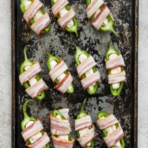 Bacon wrapped peppers on a baking sheet.