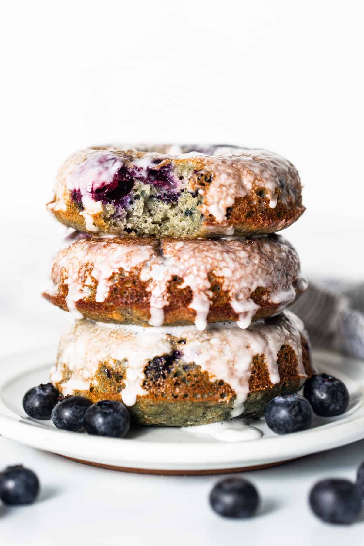 A stack of blueberry glazed donuts on a plate.