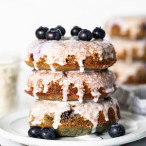 A stack of blueberry glazed donuts on a plate.