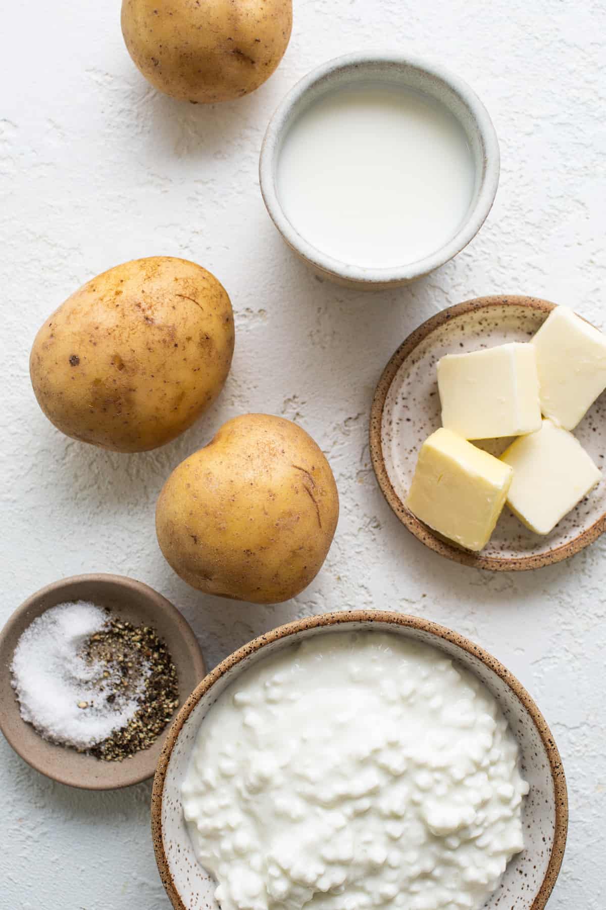 A bowl of potatoes, butter, salt and seasonings on a white background.