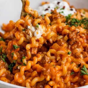 A bowl of pasta with meat sauce and sour cream.