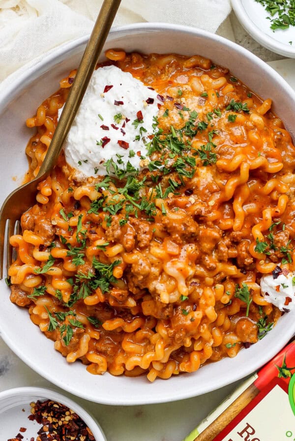 A bowl of pasta with meat sauce and sour cream.