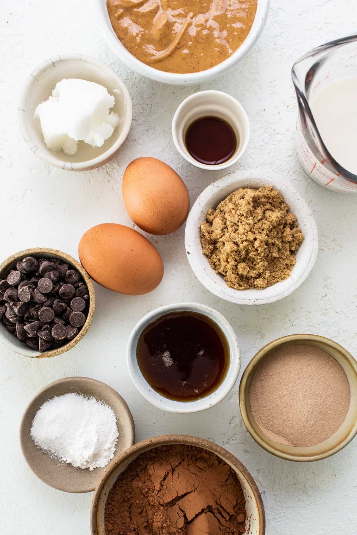 The ingredients for a chocolate cake are shown in bowls on a white background.