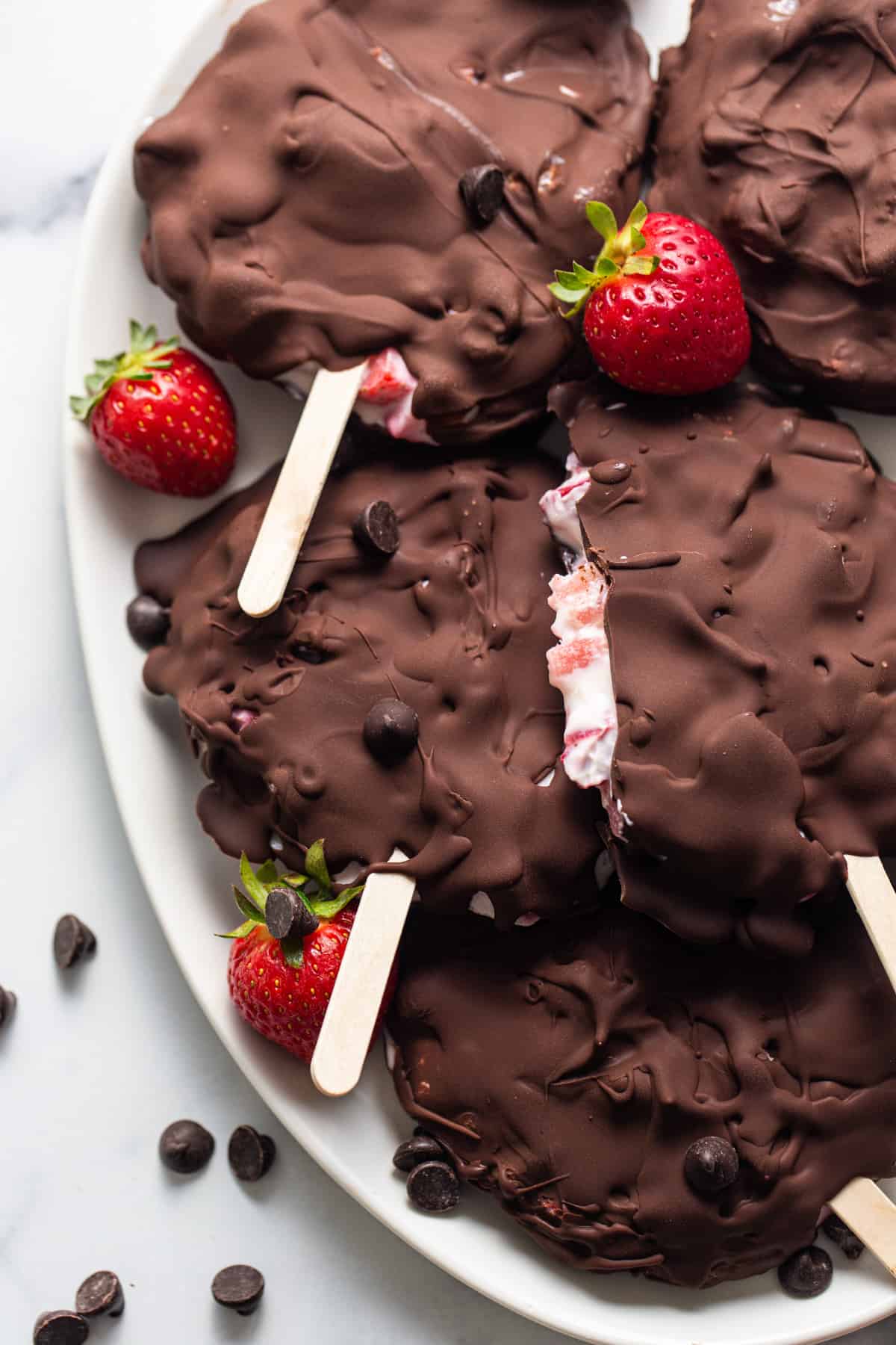 Chocolate covered strawberry popsicles on a plate.