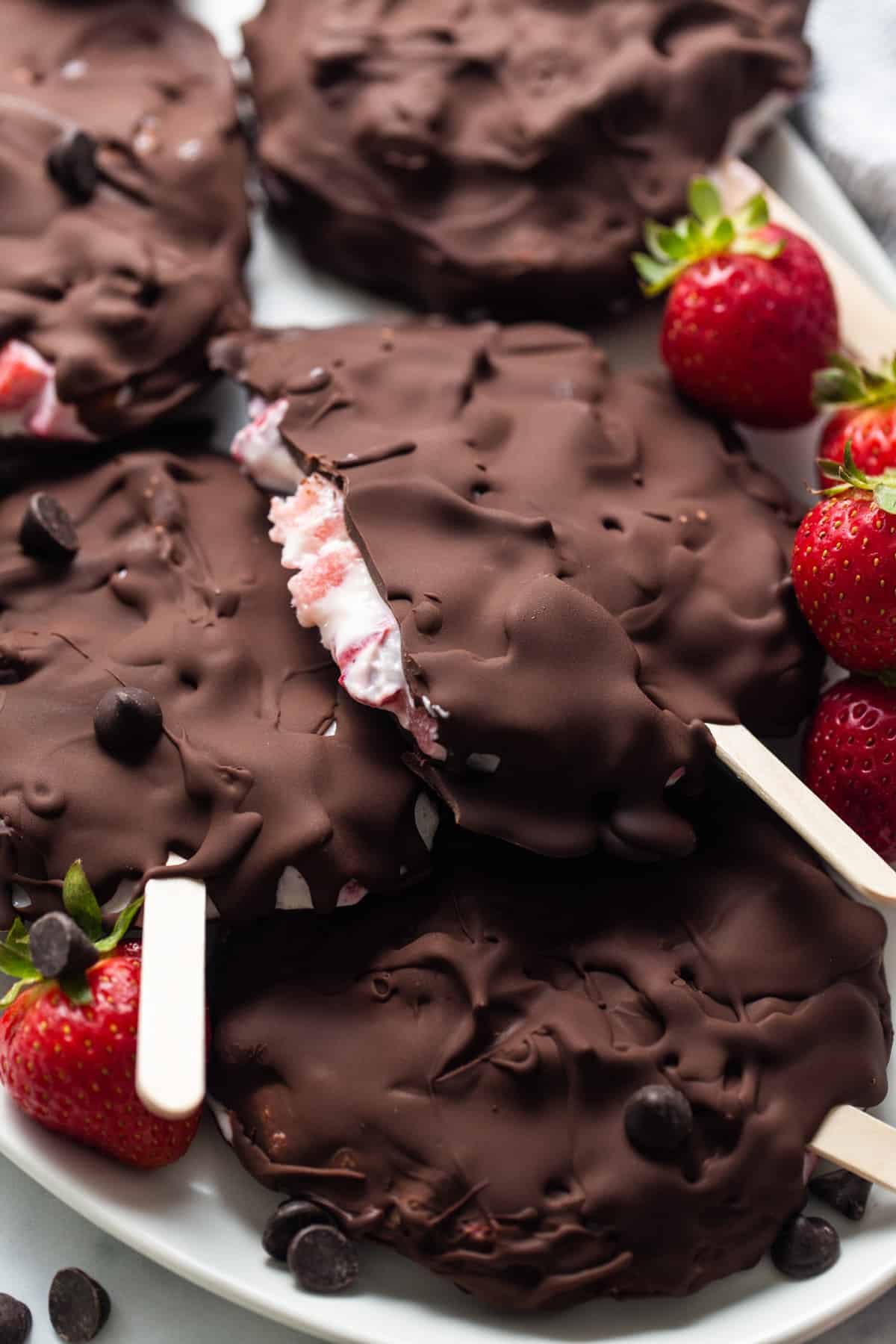 Chocolate covered strawberry popsicles on a plate.